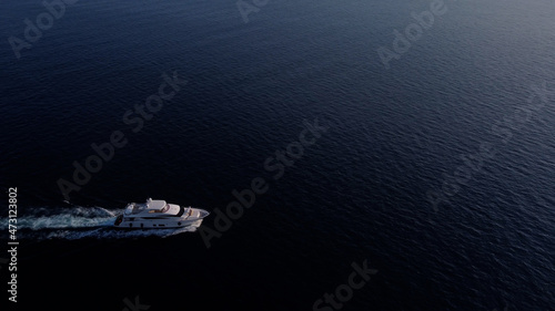 White luxury yacht sails on the ocean. Shooting from a drone as a small light sea vessel, leaving a trail of foam and waves along the sea dark water surface