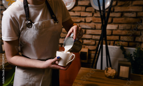 close-up of a woman pouring cream into a cup of coffee in the kitchen of a cafe-bar or restaurant. barista