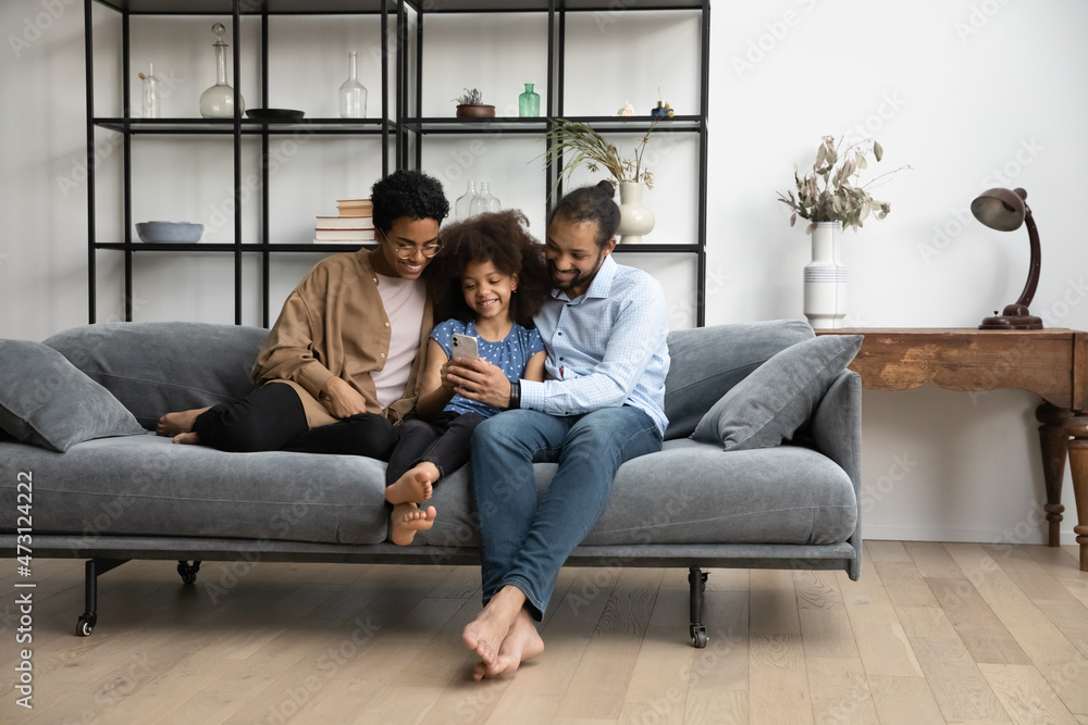 Full length addicted to modern technology bonding loving young African American couple parents using smartphone with happy cute little kid daughter, enjoying playing games or making funny photos. Full length addicted to modern technology bonding loving young African American couple parents using smartphone with happy cute little kid daughter, enjoying playing games or making funny photos.