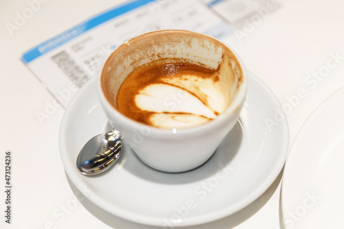 A cup with aromatic coffee and a boarding ticket for the plane on a white table. Travel and business trips. Close-up.