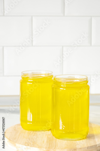 Two jars of clarified ghee butter on kitchen tile background, wooden plank.