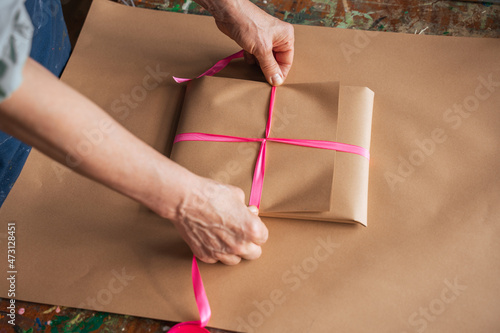 Mature woman wrapping gift with craft wrapping paper in her art room at the table