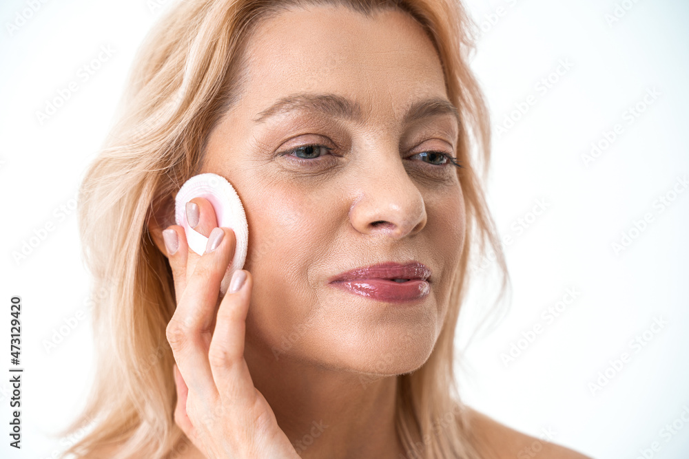 Senior attractive woman removing makeup from her face with a cotton pad