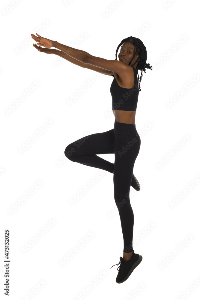African woman in black sports clothes is jumping with arms outstretched. Side view.