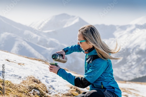 Woman pouring and drinking hot tea or coffee from thermos on winter mountain trail in Polish Tatra mountains