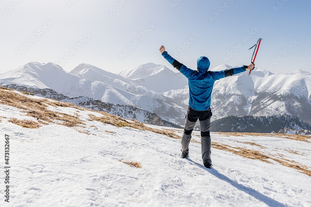 Man hiker with pickax in success pose in Polish Tatra mountains, winter mountain climbing