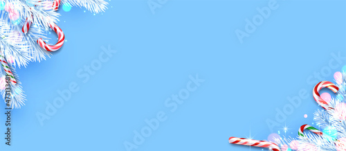 Candy canes with white fir branches frame on blue background with bokeh lights.