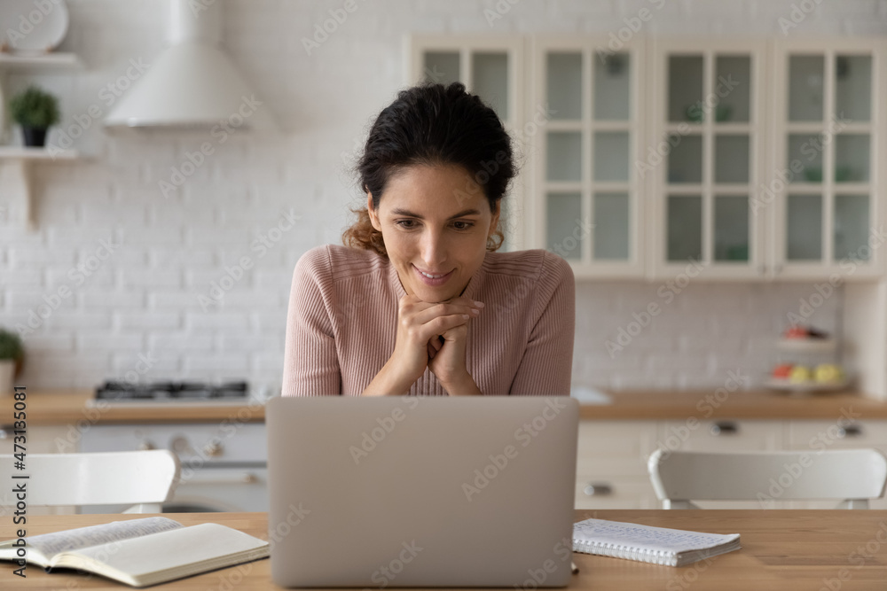 Smiling woman looking at laptop screen, working or studying online in modern kitchen at home, interested positive young female watching webinar or video training, reading good news in message Smiling woman looking at laptop screen, working or studying online in modern kitchen at home, interested positive young female watching webinar or video training, reading good news in message