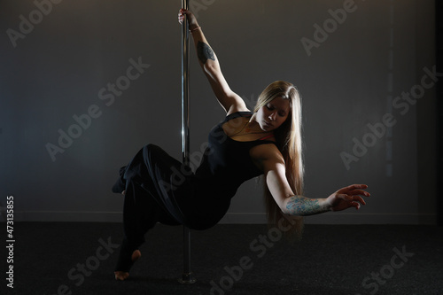 The dancer on the pylon in the studio. Girl doing exercises on a sports equipment.