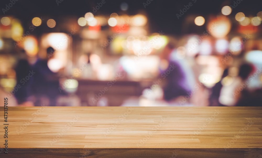 Selective focus.Wood table top with blur light bokeh in dark night cafe,restaurant background.