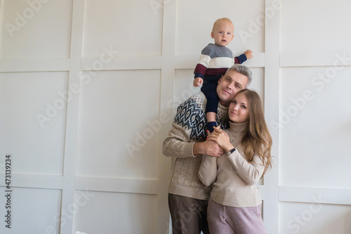 Happy young family with toddler son on grey apartment wall background with copy space. Rental, moving, mortgage concept