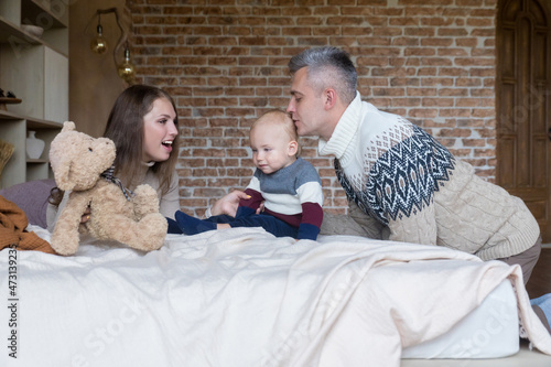 Affectionate young family having fun playing with little son on bed at home. Happy parenthood concept