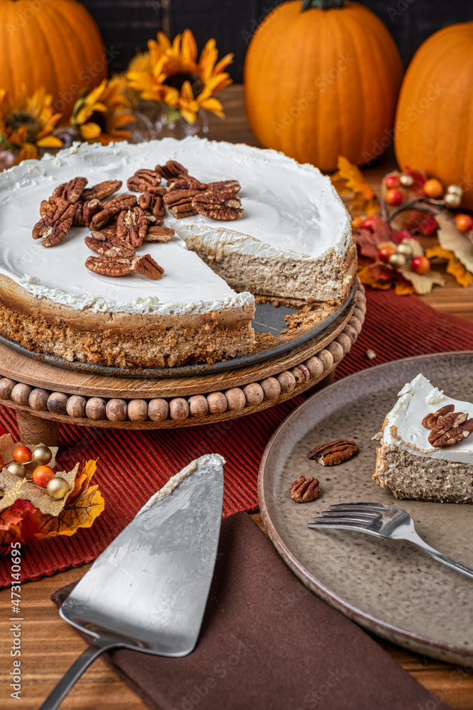 Fototapeta premium Slice of homemade pumpkin cheesecake served on a plate with a scatter of pecans to top it off.