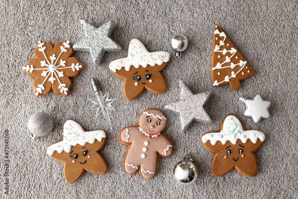 Flat lay set of ginger and cinnamon cookies: gingerbread man, snowflakes, stars decorated with icing on grey background with xmas toys. Sweet present for Christmas day.