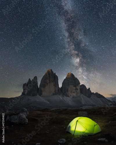Green tent lighted from the inside against the backdrop of incredible starry sky and Three Peaks of Lavaredo mountains. National Park Tre Cime di Lavaredo, Dolomites, Italy. Landscape photography © Ivan Kmit