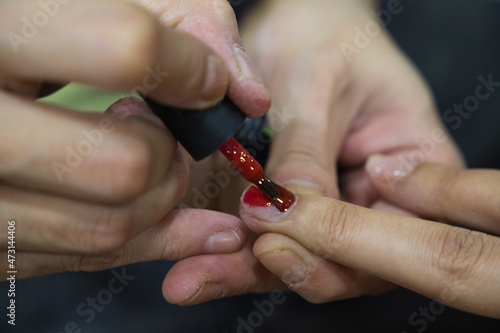 Manicure. Close-up of beautiful woman hands polishing nails with red nail polish in beauty salon. Close-up of beautician hand painting client s nails. Beauty concept. High Resolution.
