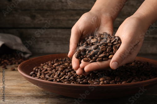 Woman taking pile of aromatic roasted coffee beans from bowl at wooden table  closeup