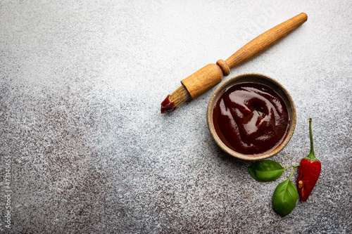 Tableau sur toile Barbecue sauce in a saucer with basting brush over gray stone table, top view with copy space