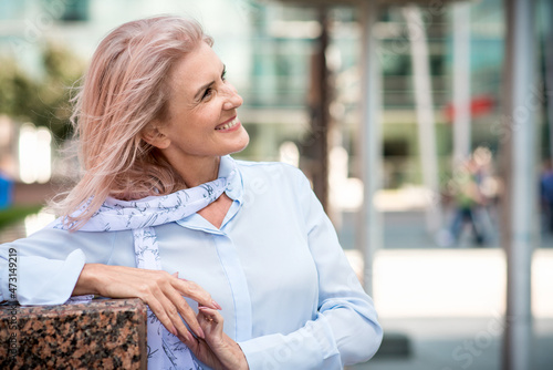 Portrait of attractive elderly woman with gray hair in casual clothes in the city. Freelance successful business lady posing on the street