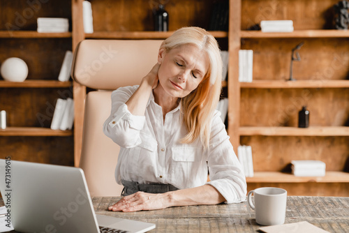 Caucasian middle-aged mature businesswoman tutor teacher ceo boss suffering from neck pain, overworked, sedentary lifestyle problems at work place. photo