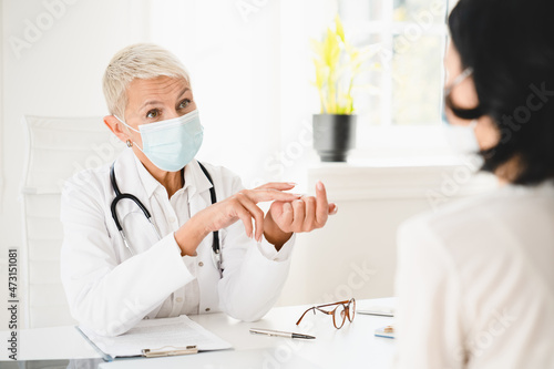 Senior female doctor gynecologist in protective face mask against coronavirus Covid 19 talking with patient about diagnosis recovery, giving prescriptions test results in hospital photo