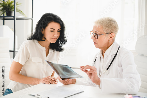 Radiogram. Caucasian senior female doctor general practitioner showing x-ray lungs photo to female patient, explaining diagnosis, symptoms at hospital photo