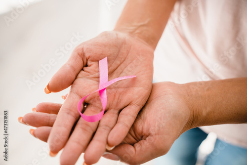 Close up cropped shot of women`s hands holding pink ribbon in support of breast cancer. World cancer day. Charity organization, fighting tumors oncology