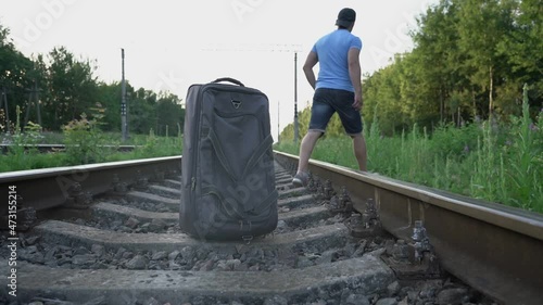 adult male traveler put road bag on railway and went into grass to urinate outdoors on summer day photo