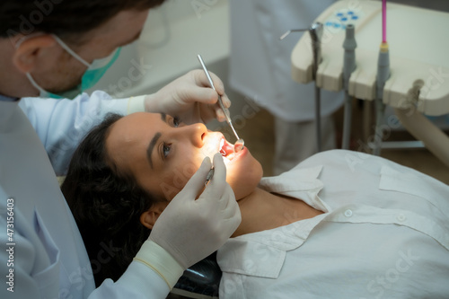 Dentist holding a tooth mirror and dental pick are performing dental exam on a patient in dental clinic