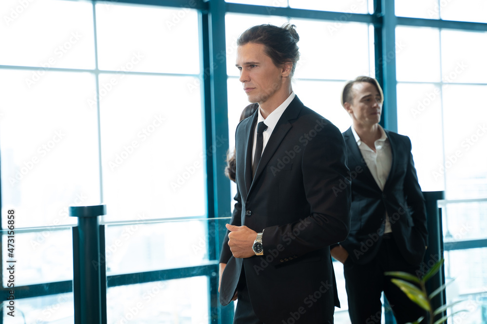 Young male employee in formal clothes standing in the office,Group of people talking behind. Young male employee in formal clothes standing in the office,Group of people talking behind.