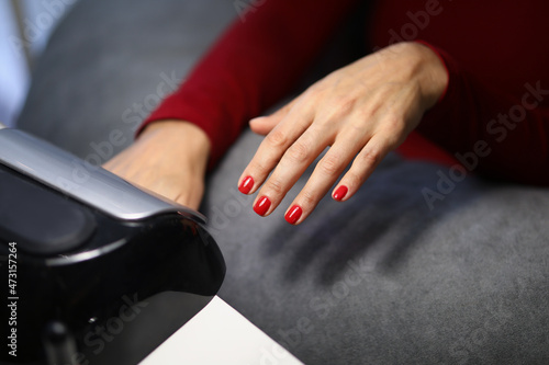 Woman client putting hand with fresh red nails under lamp to dry it