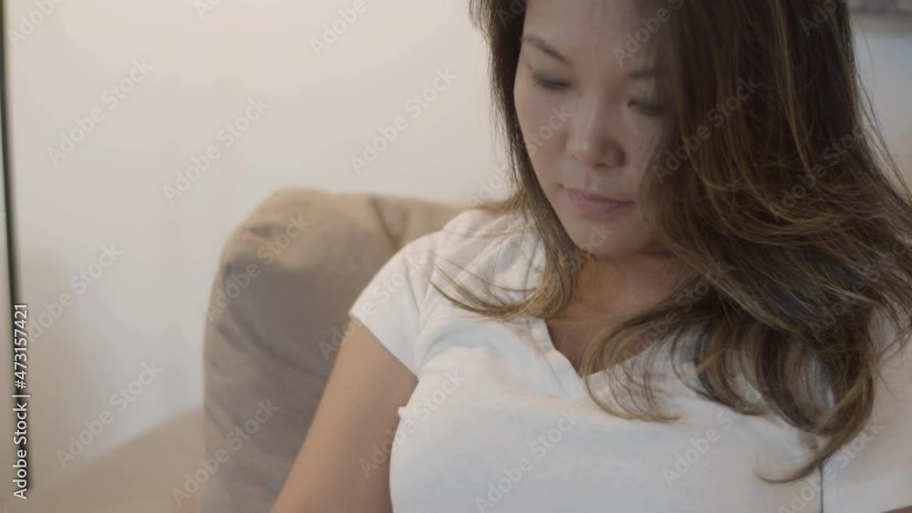 Medium shot of charming woman looking at tablets screen at home. Front view of focused Japanese girl sitting on sofa with tablet, having rest after working day. Technology, relaxation concept Medium shot of charming woman looking at tablets screen at home. Front view of focused Japanese girl sitting on sofa with tablet, having rest after working day. Technology, relaxation concept