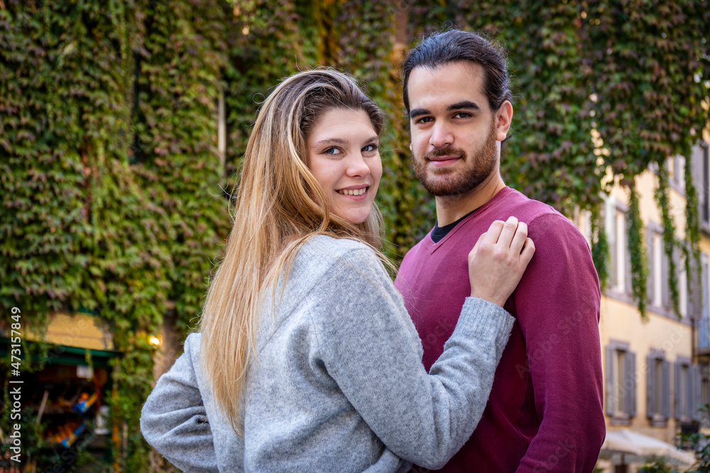 Young couple traveling to Rome. Beautiful blonde woman hugs her boyfriend. In the background, a street in the historic center with an ivy-covered building. Young couple traveling to Rome. Beautiful blonde woman hugs her boyfriend. In the background, a street in the historic center with an ivy-covered building.