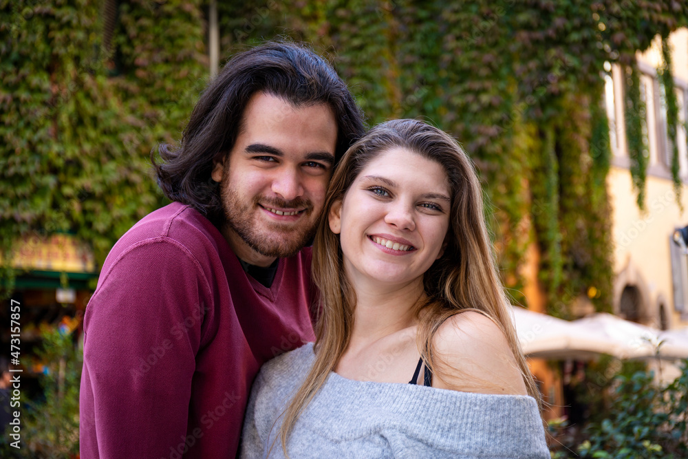 Naklejka premium Beautiful couple traveling to Rome. Young couple takes a selfie in a street in the historic center. In the background a building covered with ivy.