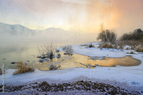 Winter landscape, river with icy banks, mountains in the fog.