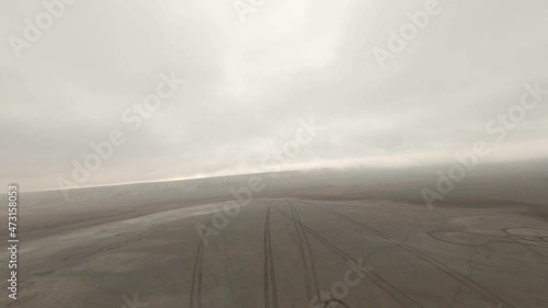 Buggy suv automobiles drive along dried salt lake leaving traces on yellow sand under grey cloudy sky FPV chase sport drone view photo