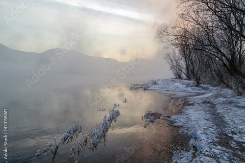 Winter landscape, river with icy banks, mountains in the fog.