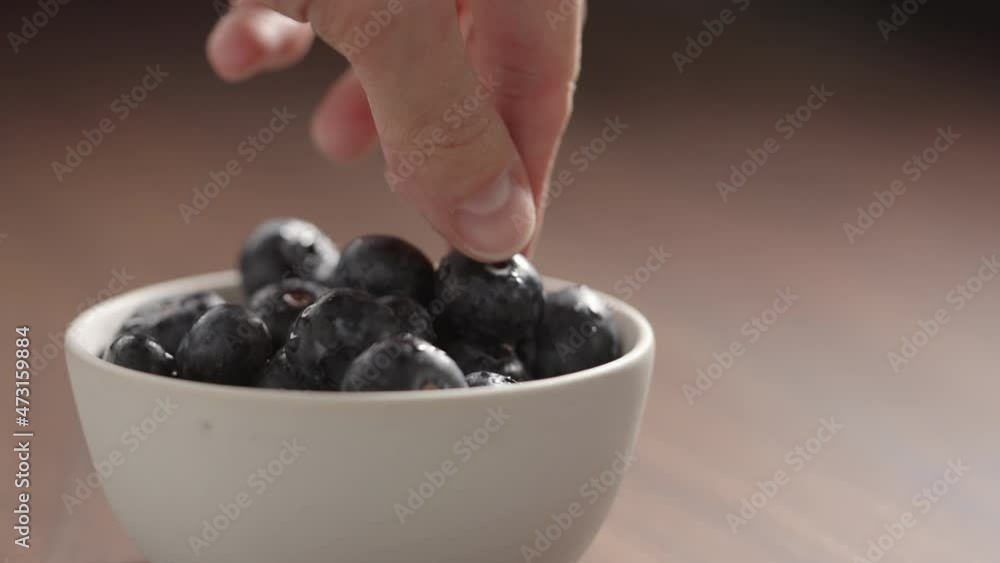 Slow motion fresh washed blueberries picked by man hand from white bowl Slow motion fresh washed blueberries picked by man hand from white bowl