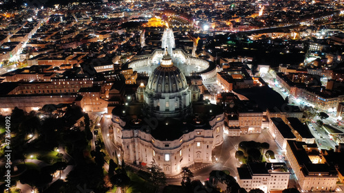 Aerial drone night shot of iconic masterpiece Saint Peter Basilica and whole illuminated city of Vatican the biggest church in the world, Metropolitan city of Rome, Italy