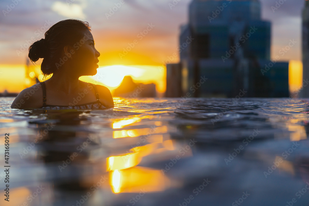 Black silhouette of asian woman splash water on summer vacation holiday relaxing in infinity swimming pool with blue sea sunset view with high rise skyscape urban downtown Healthy happiness lifestyle Black silhouette of asian woman splash water on summer vacation holiday relaxing in infinity swimming pool with blue sea sunset view with high rise skyscape urban downtown Healthy happiness lifestyle