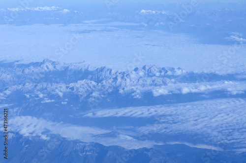 Beautiful window view of blue sky, fluffy clouds and Alps mountains from passenger seat on airplane. Travel and air transportation. Holidays