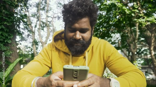 Man with a yellow outfit using a smartphone in a park,Indian male model with green background	

