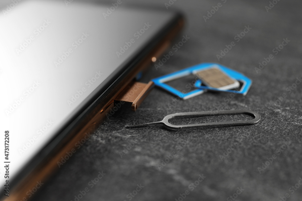 SIM card, mobile phone and ejector tool on grey table, closeup SIM card, mobile phone and ejector tool on grey table, closeup