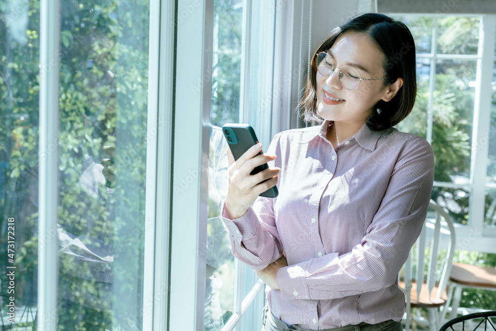 Obraz premium Asian woman wear glasses Working style, looking at the phone in the room express smile, feel good in the day