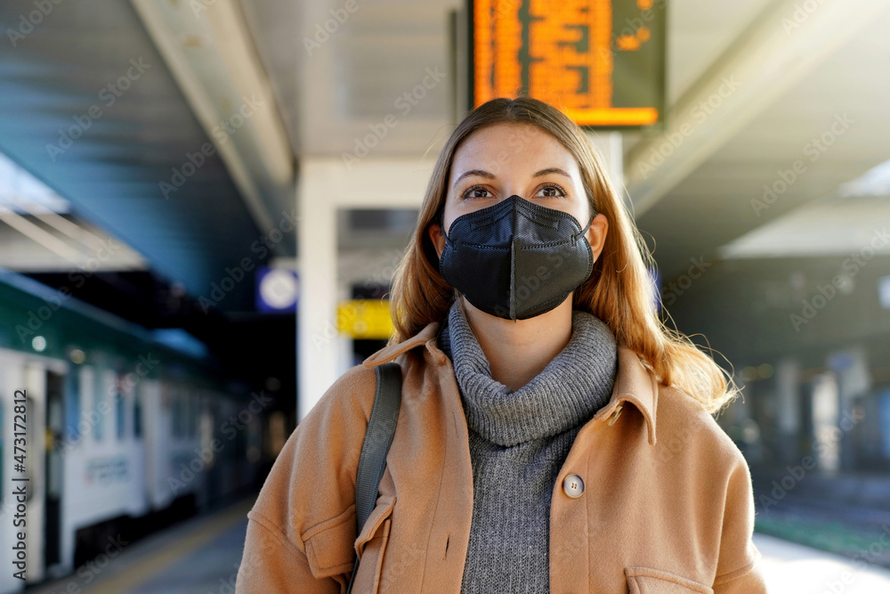 Beautiful woman wearing black face mask FFP2 KN95 in train station with timetables on background Beautiful woman wearing black face mask FFP2 KN95 in train station with timetables on background