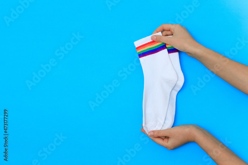 hand with pair of white cotton socks with rainbow stripes on blue background isolate
