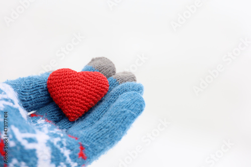 Red heart on palm of hand in warm knitted glove against the white snow. Concept of a romantic love, Valentine's day or charity
