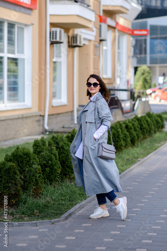 a fashionable girl in trousers, a raincoat, a blouse with a handbag walks around the city. Business concept