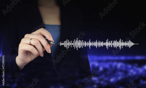 Audiobook audio technology. Digital sound track on hand. Hand holding digital graphic pen and drawing digital hologram sound track, wave sign on city dark blurred background.