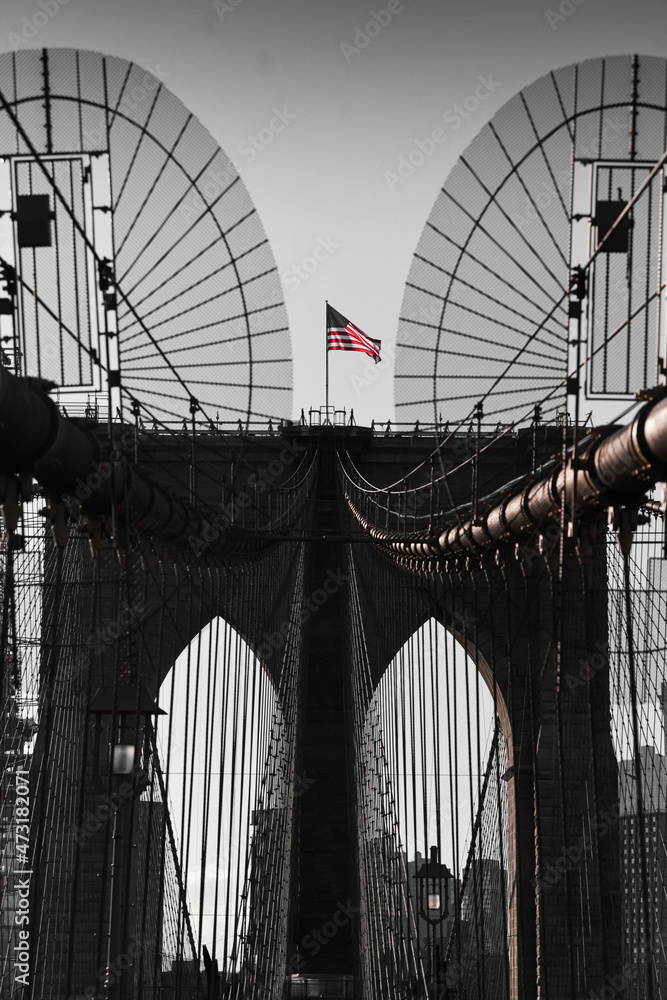 Obraz premium The national flag of United States of America winding on top of Brooklyn Bridge landmark from Manhattan. One of the most visited places in America. Symbol of patriotism.